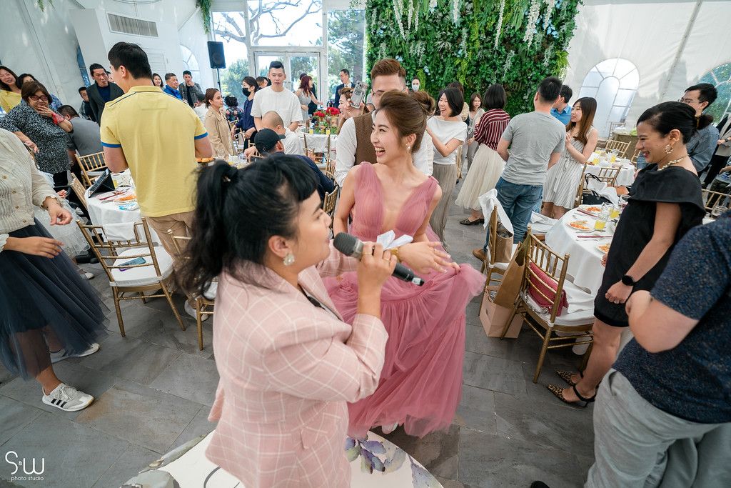 Reception guests mingling and taking photos in a bright indoor venue decorated with greenery.