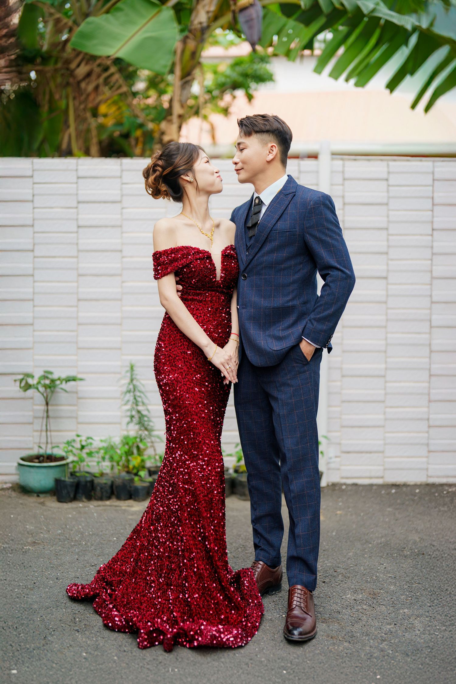 A couple in a red sequin dress and navy suit share romantic moments in a garden photoshoot series.