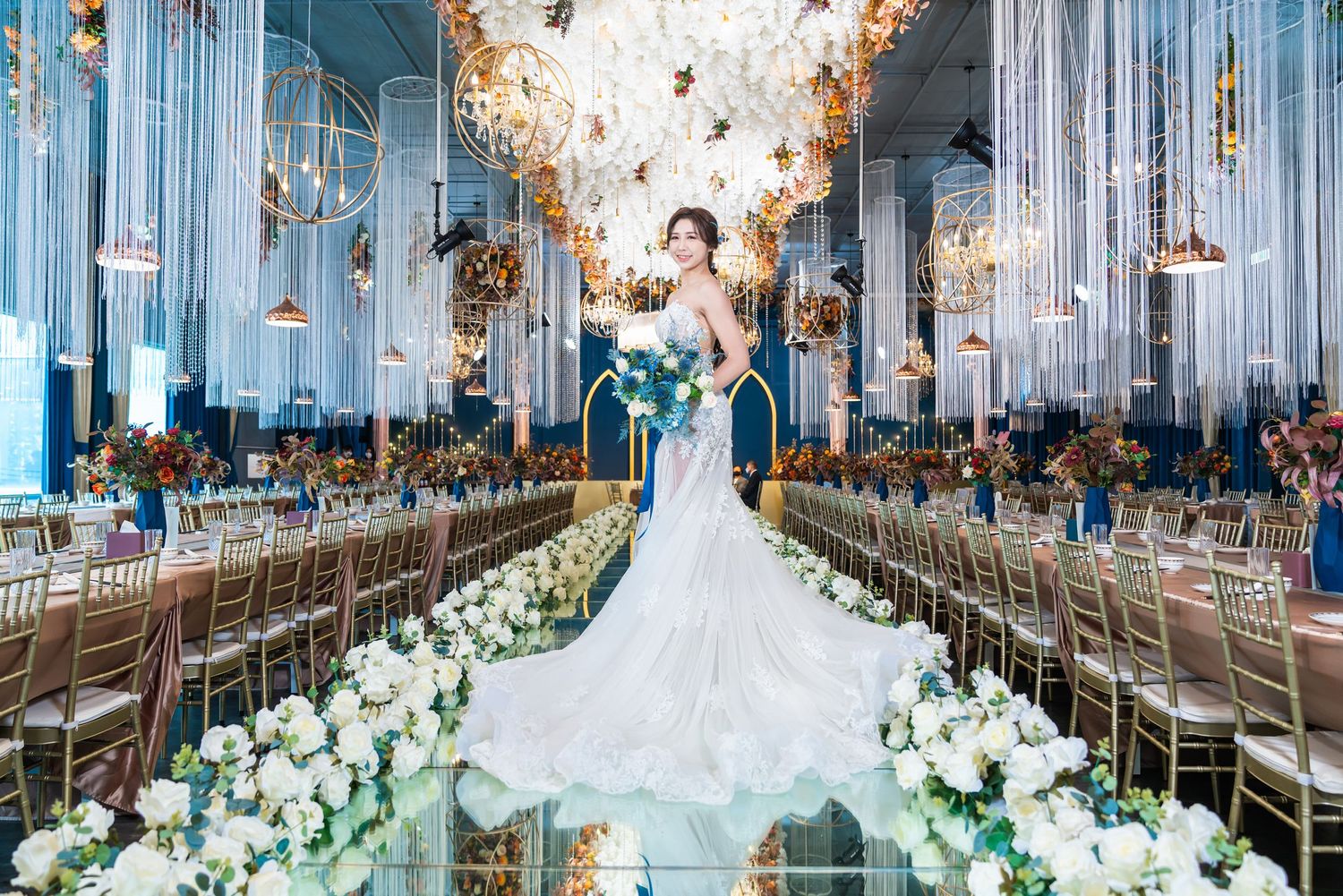 Elegant wedding reception venue with mirrored walls, long dining tables, floral arrangements and white decorative elements.
