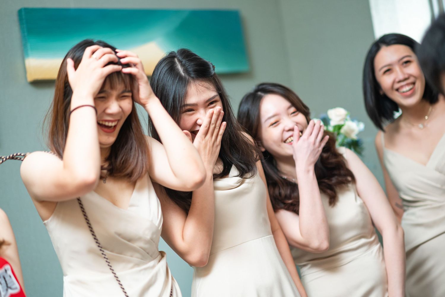 Four bridesmaids in matching cream-colored dresses share a candid laughing moment at a wedding celebration.