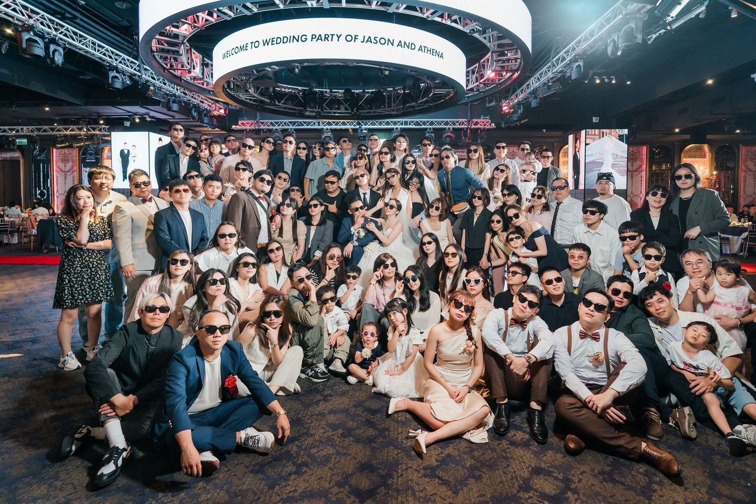 A large group of people posing together at a corporate event in a modern venue with circular lighting overhead.
