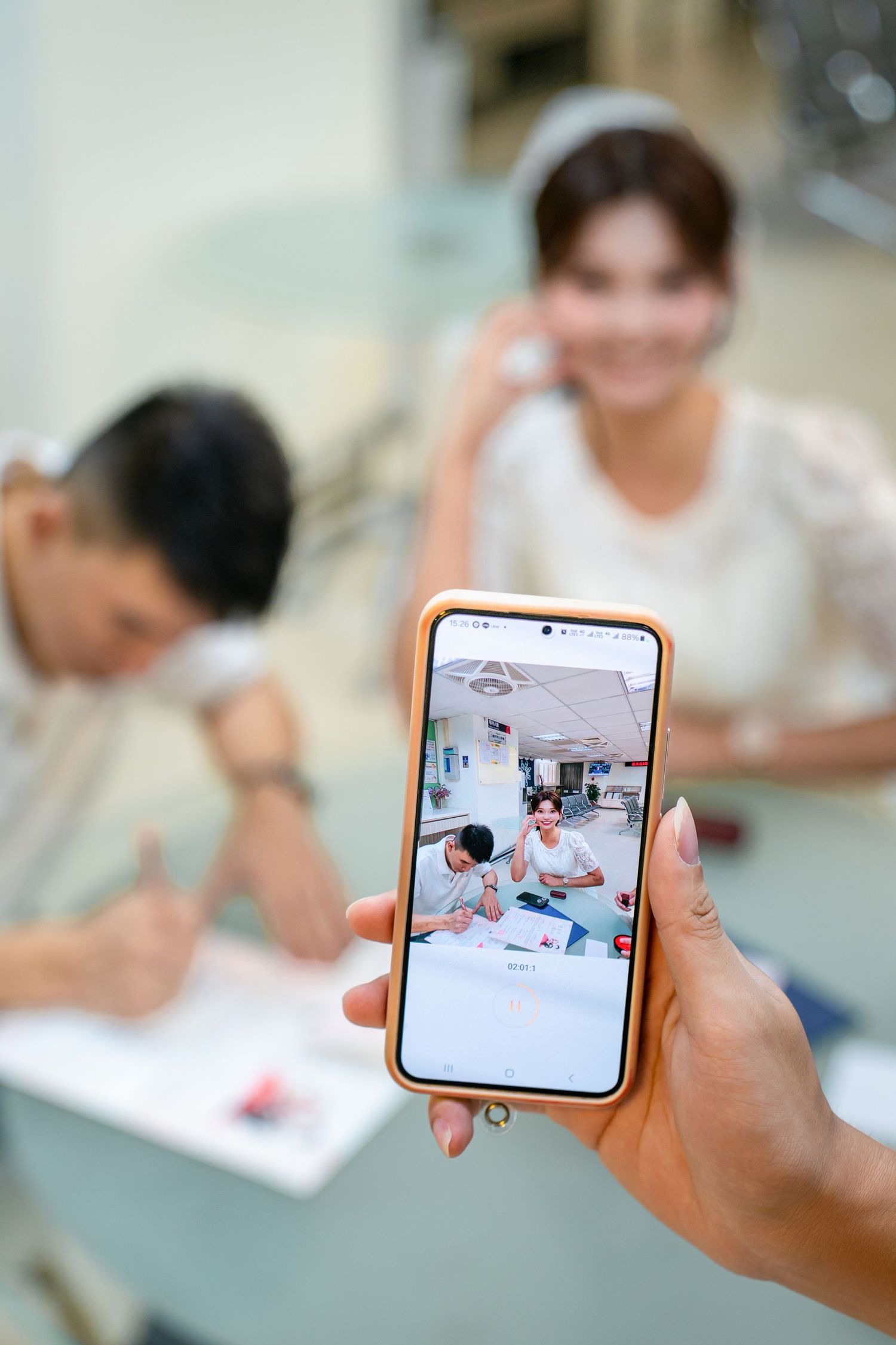 Hand holding smartphone capturing students working at desks in classroom setting.