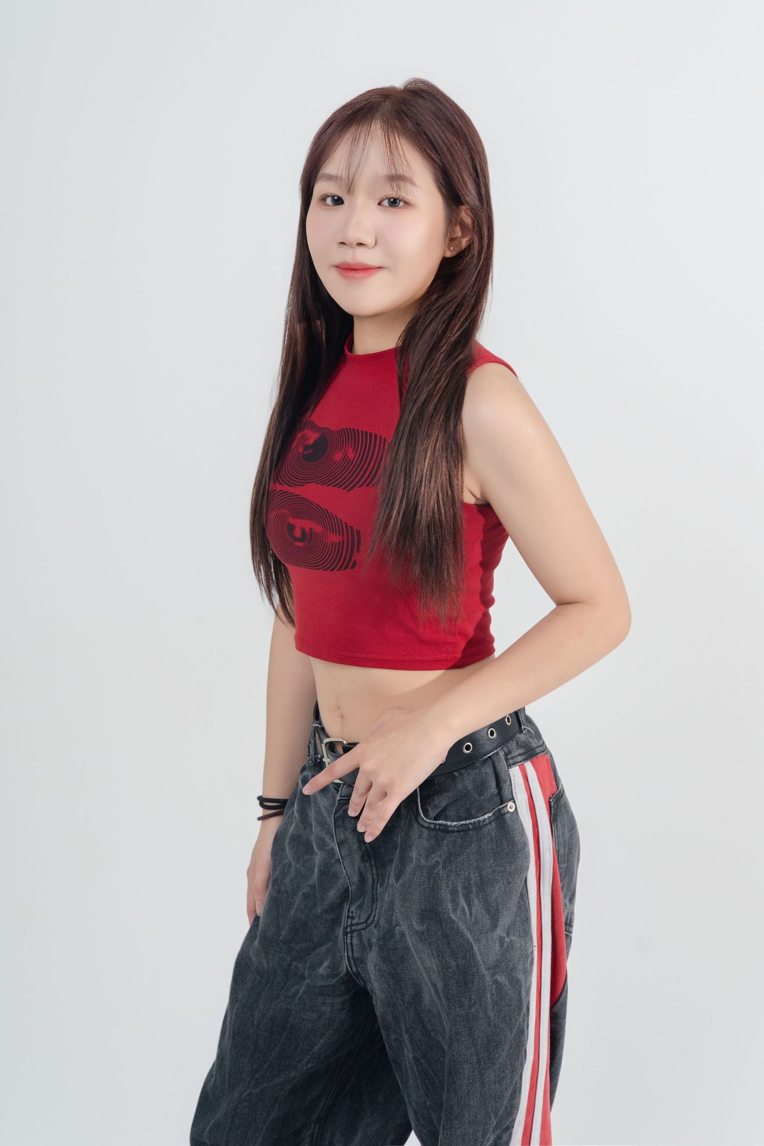 A person in a red sleeveless top and gray jeans with red side stripes poses against a white background.