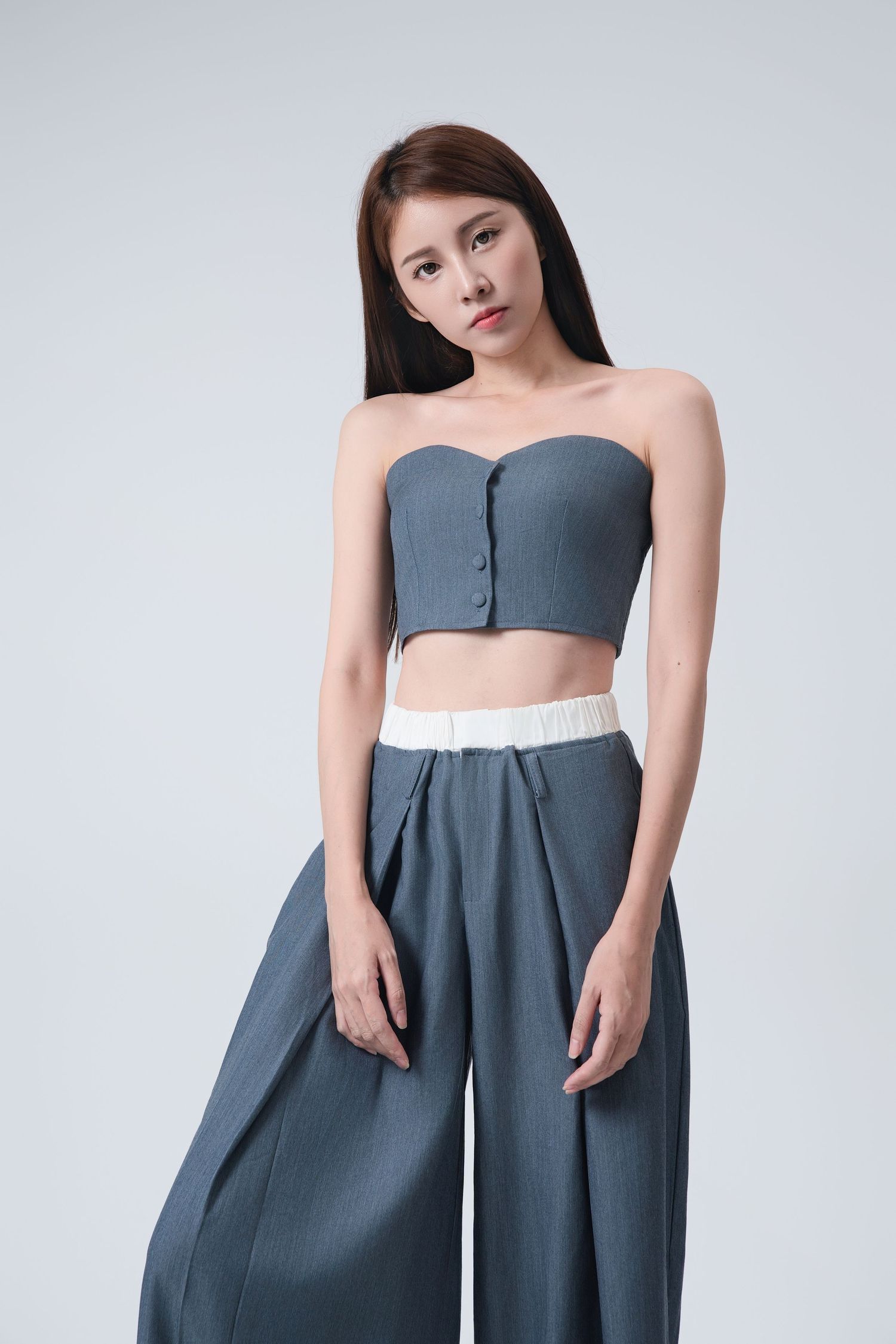 Woman wearing a modern strapless grey dress with high waistline and pleated skirt details.