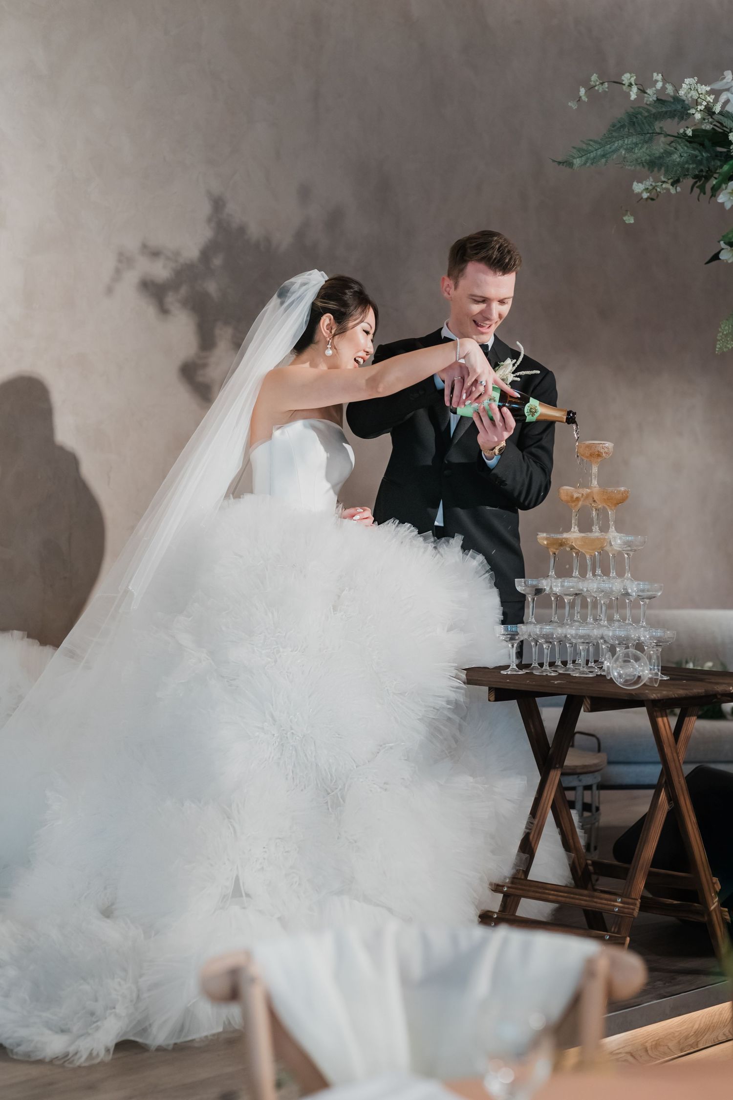 Newlyweds celebrate with a champagne tower during their wedding reception amidst elegant smoke effects.