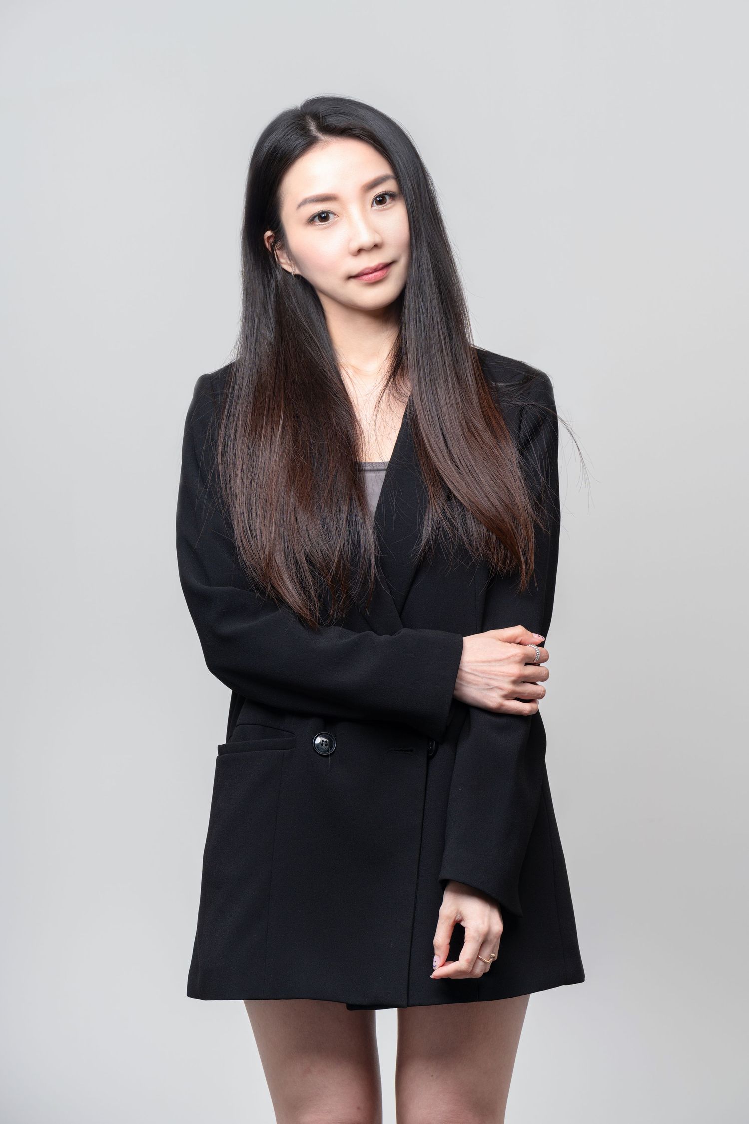 Professional studio portrait of a person in a black blazer dress against a gray background.