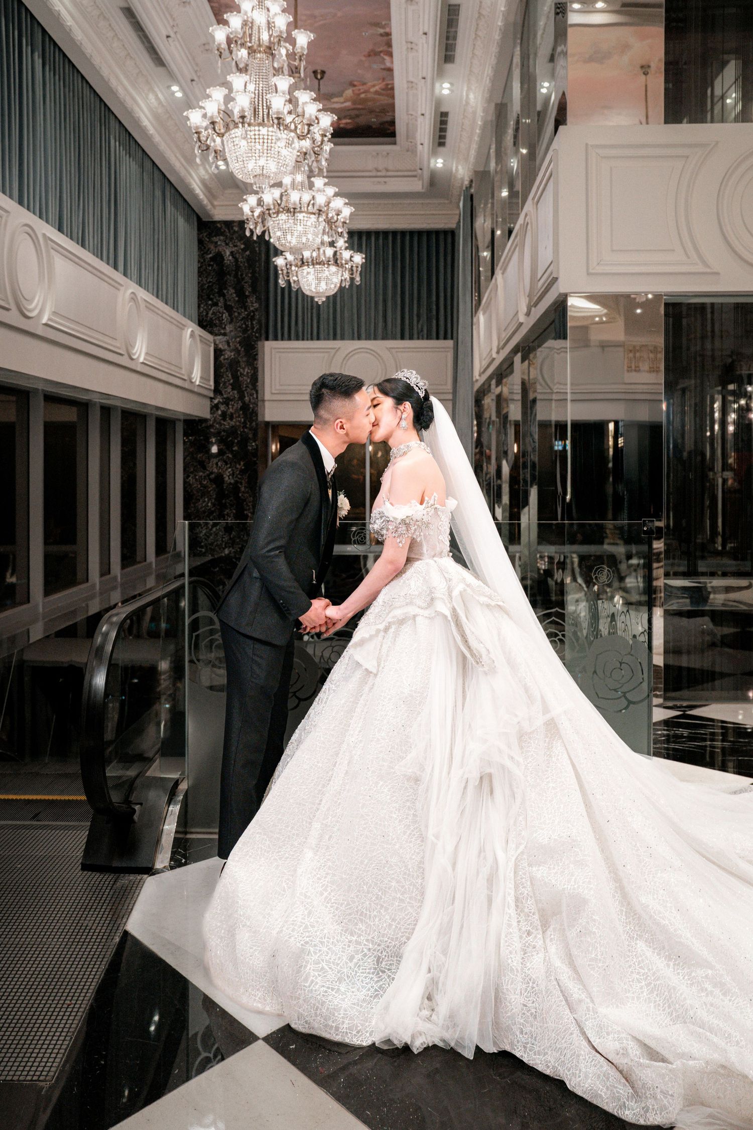 Elegant wedding couple shares romantic moments under crystal chandeliers in a luxurious ballroom setting.