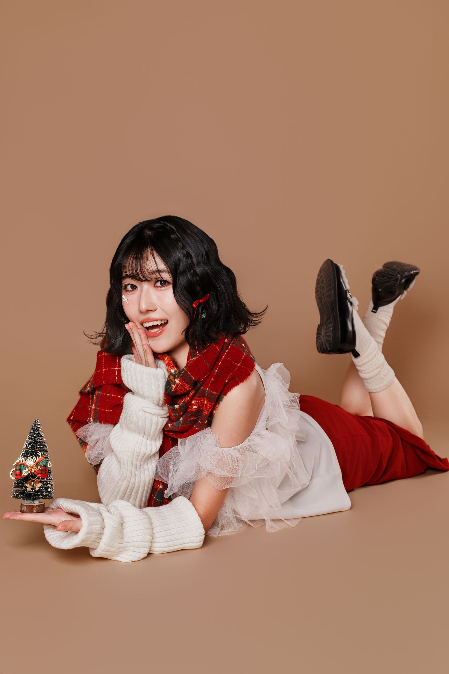 A person in a white sweater and red skirt lies on a brown backdrop in a series of playful holiday-themed poses.