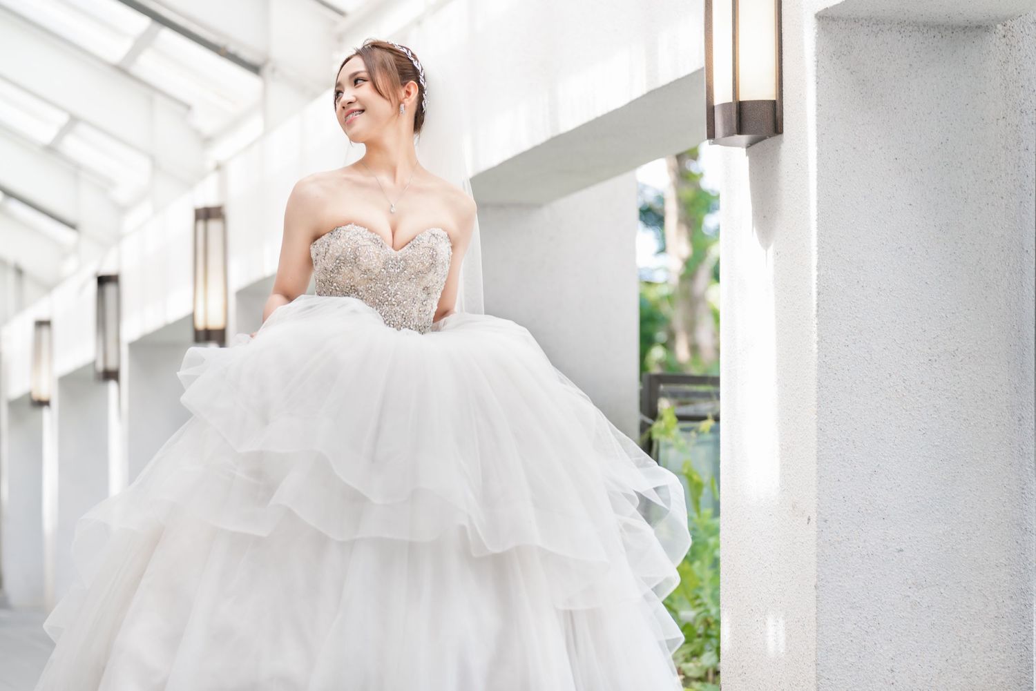 Bride in sweetheart neckline ballgown poses in bright indoor corridor with modern lighting.