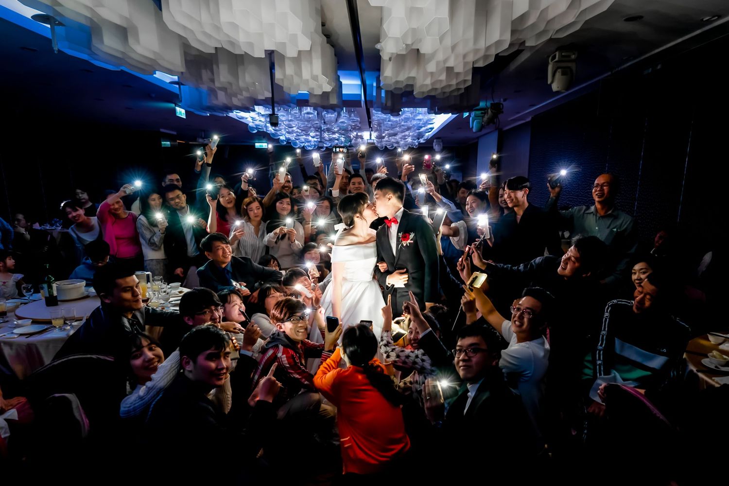 Crowded nightclub scene with people holding up phone lights in a dark space creating an atmospheric ambiance.
