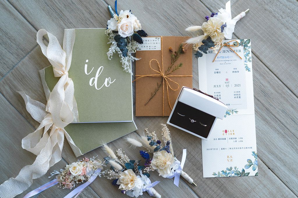 Wedding details flatlay with vow book, invitation, rings and delicate floral decorations.