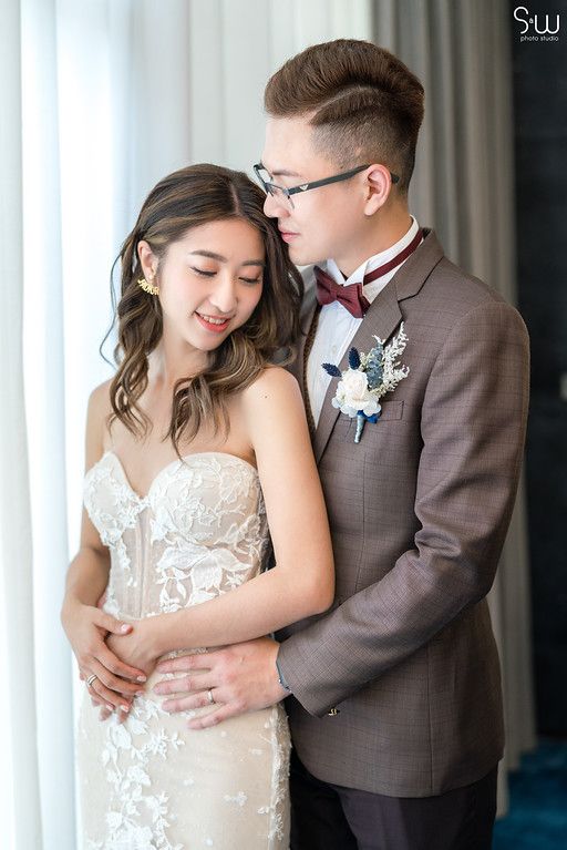 Intimate wedding portrait with couple in elegant attire against sheer curtained window.