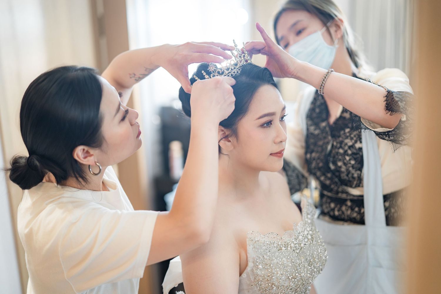 Wedding day preparation scene with stylists adjusting a sparkly strapless bridal gown and accessories.