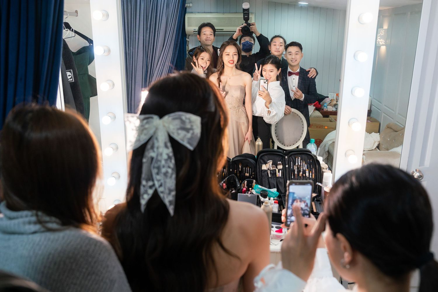Behind the scenes view of a person taking a photo on their phone at a wedding preparation gathering in a dressing room.
