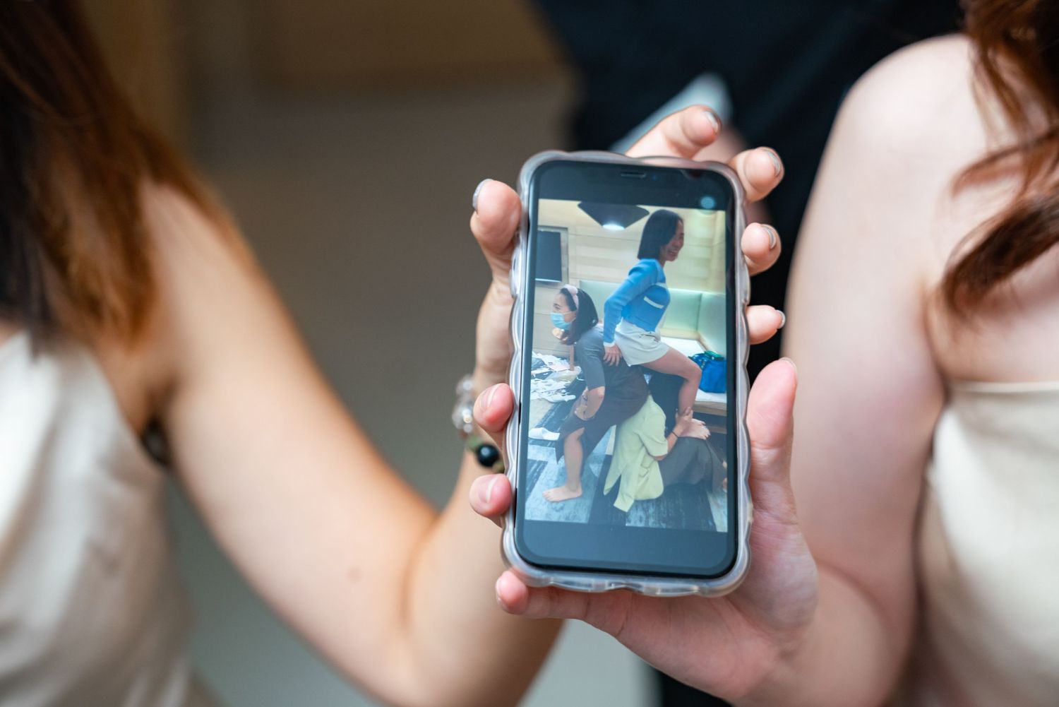 Person holding a smartphone displaying a photo of people having fun on a bright sunny day.