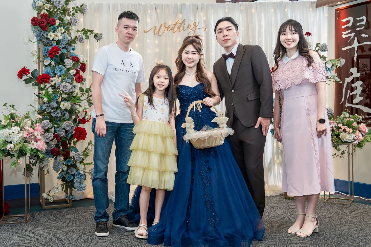 A group of people dressed in formal attire gather for photos at an event with floral decorations.