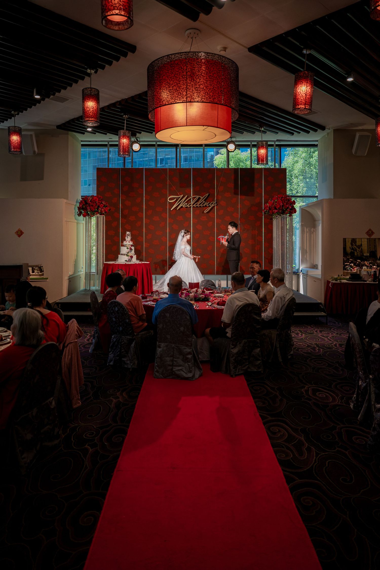 Red-themed wedding reception venue with Chinese lanterns illuminating a spacious room and red carpet aisle.