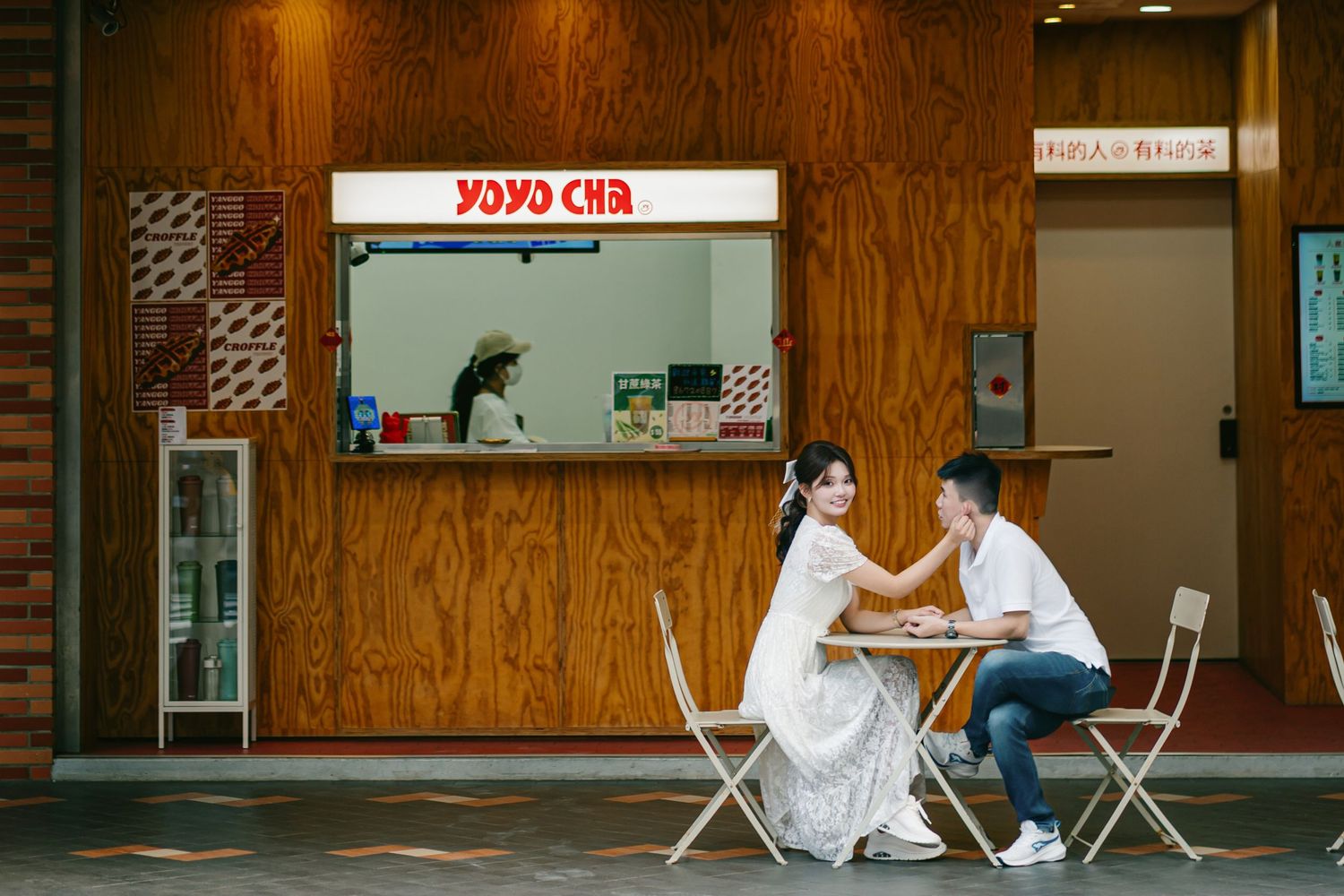 A small cafe storefront with a neon sign and glass windows displays a cozy interior with wooden paneling.