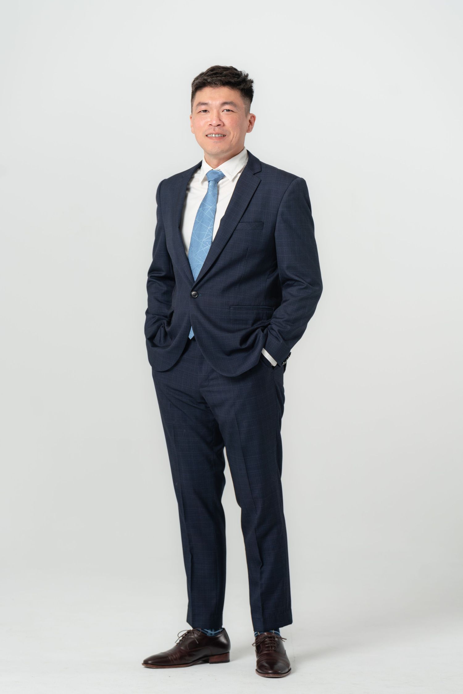 Professional portrait of someone in a dark business suit and blue tie standing against a white studio background.
