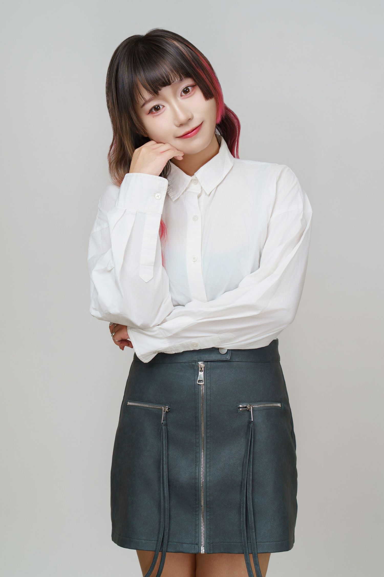 A person in a white button-up shirt and dark pleated miniskirt poses in a series of casual studio shots.
