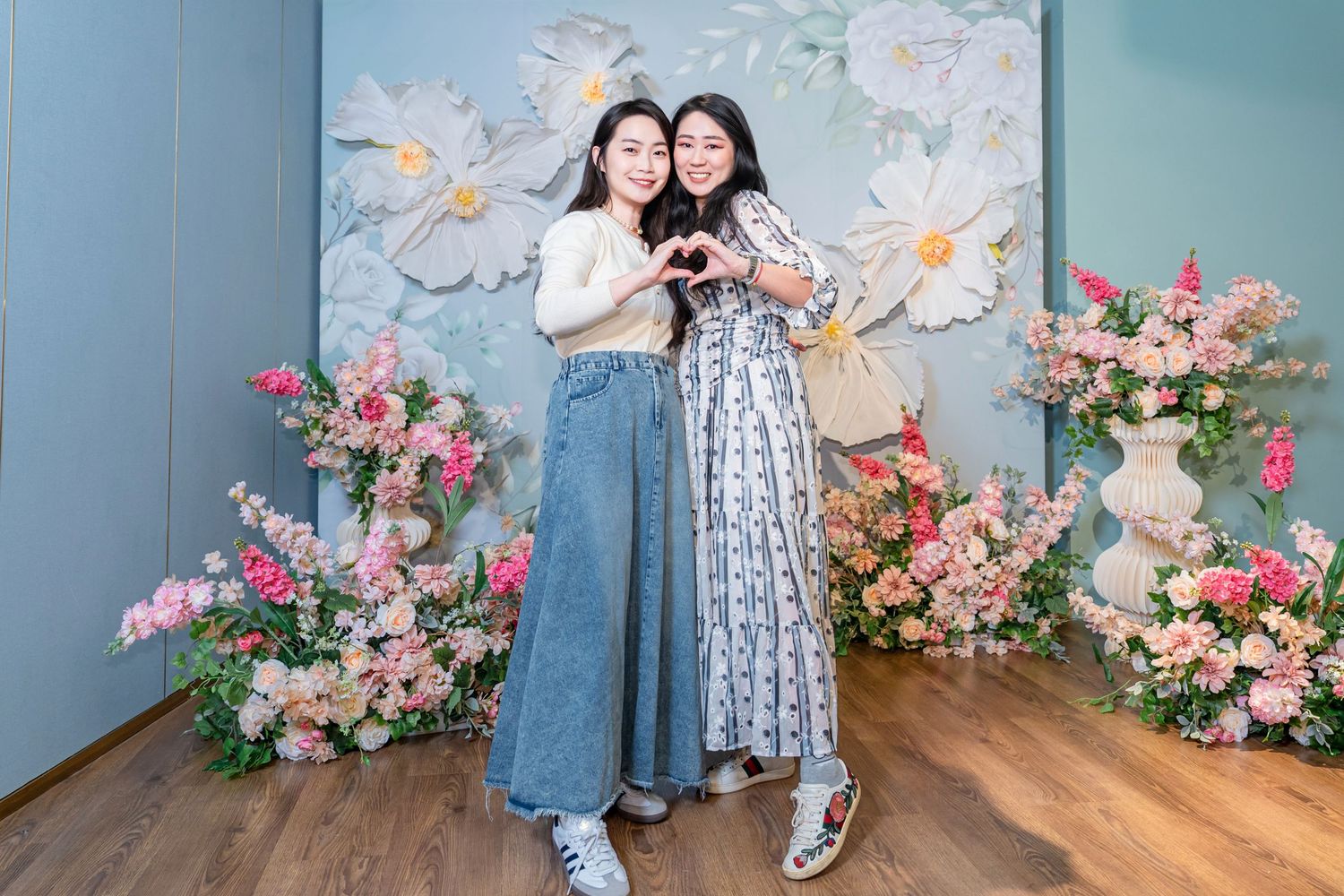 A photo collage showing people posing against a blue wall with pink floral decorations in a studio setting.