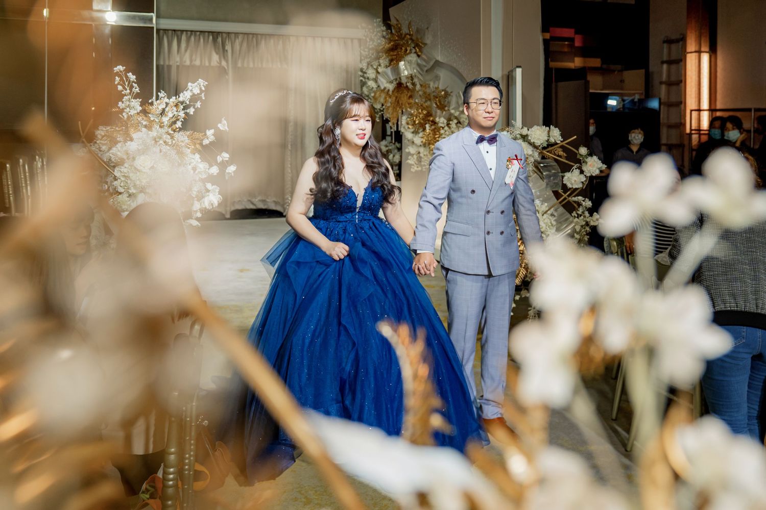 A couple in blue and grey attire dancing together at an elegant indoor venue with romantic lighting.