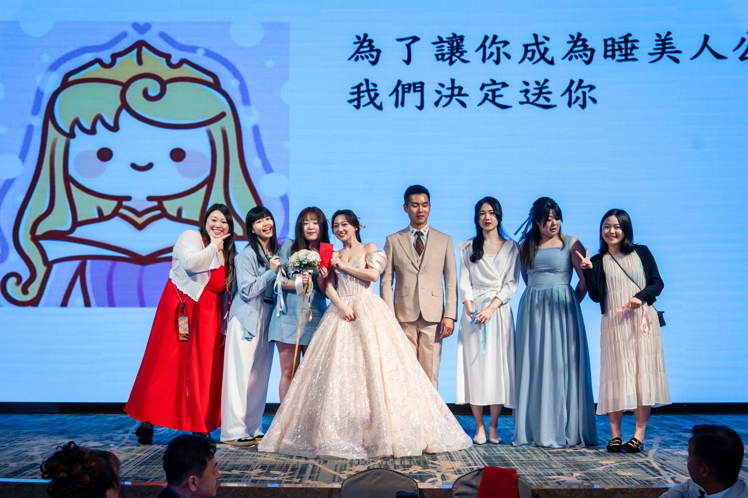 Wedding party poses on stage with Chinese text backdrop at formal celebration event.
