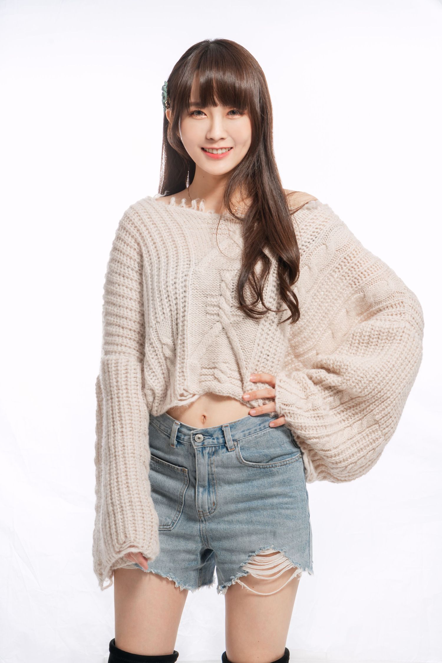 A casual street style look featuring a cream knit sweater, distressed denim shorts and black knee-high boots.
