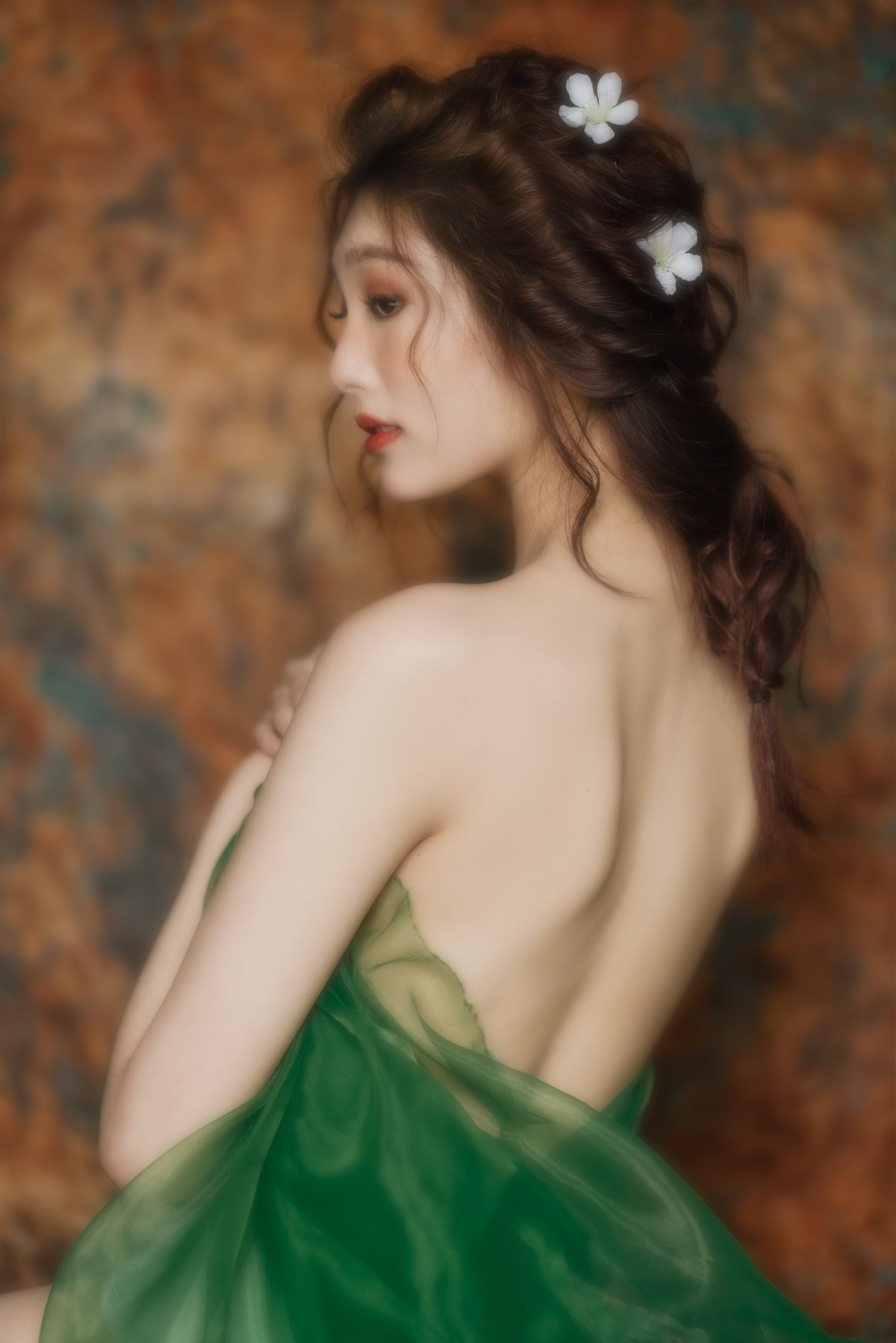 Artistic portrait of a feminine figure in emerald green dress with delicate white flowers in dark hair against textured backdrop.