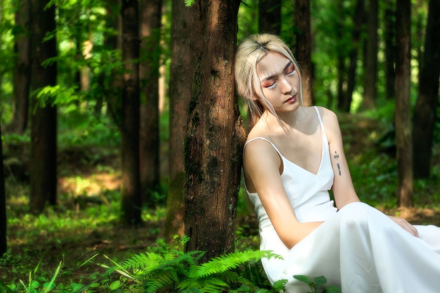Woman in a white dress sitting on mossy ground in a bright green forest.