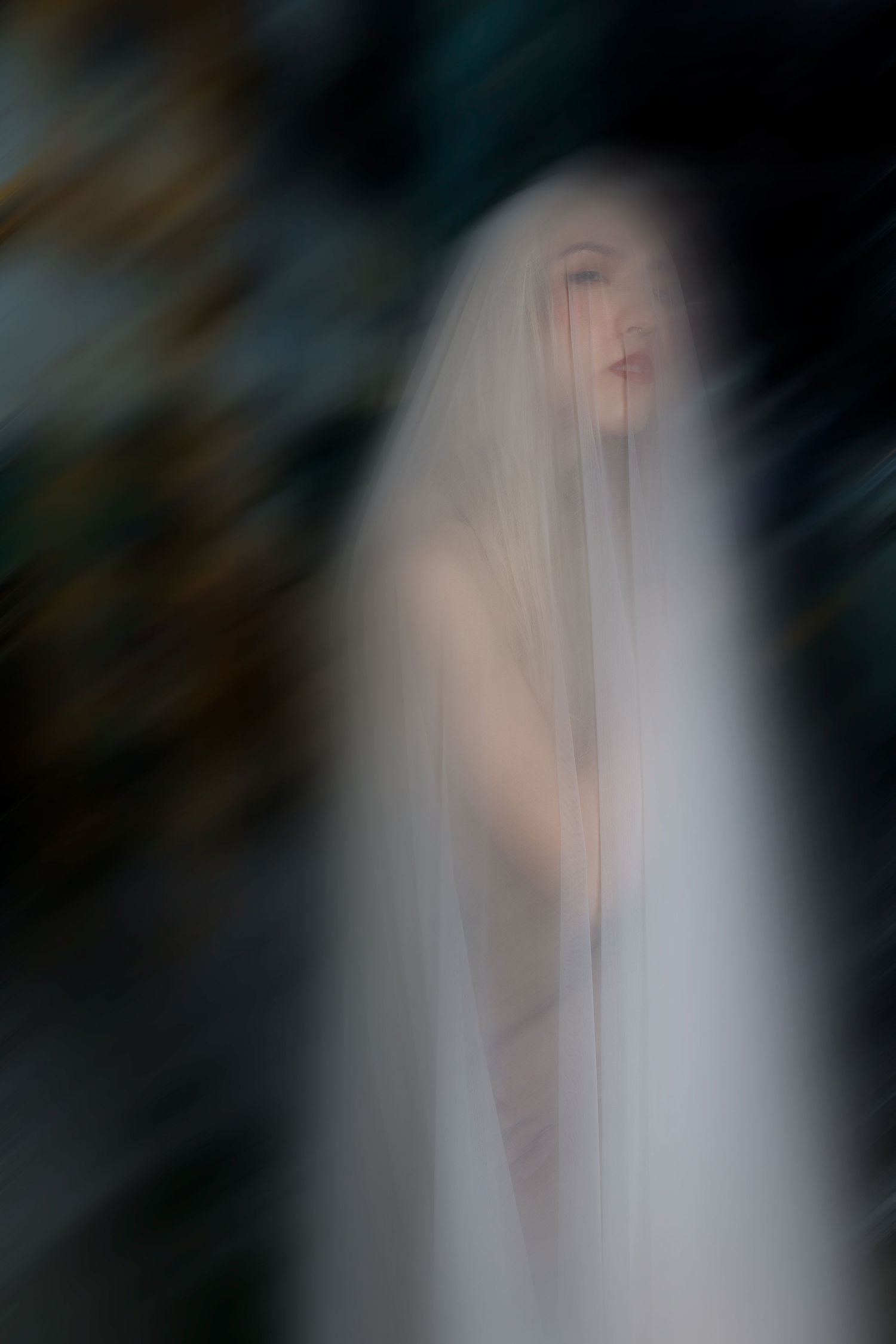Ethereal artistic portrait in soft focus showing a figure draped in white veil against dark background.