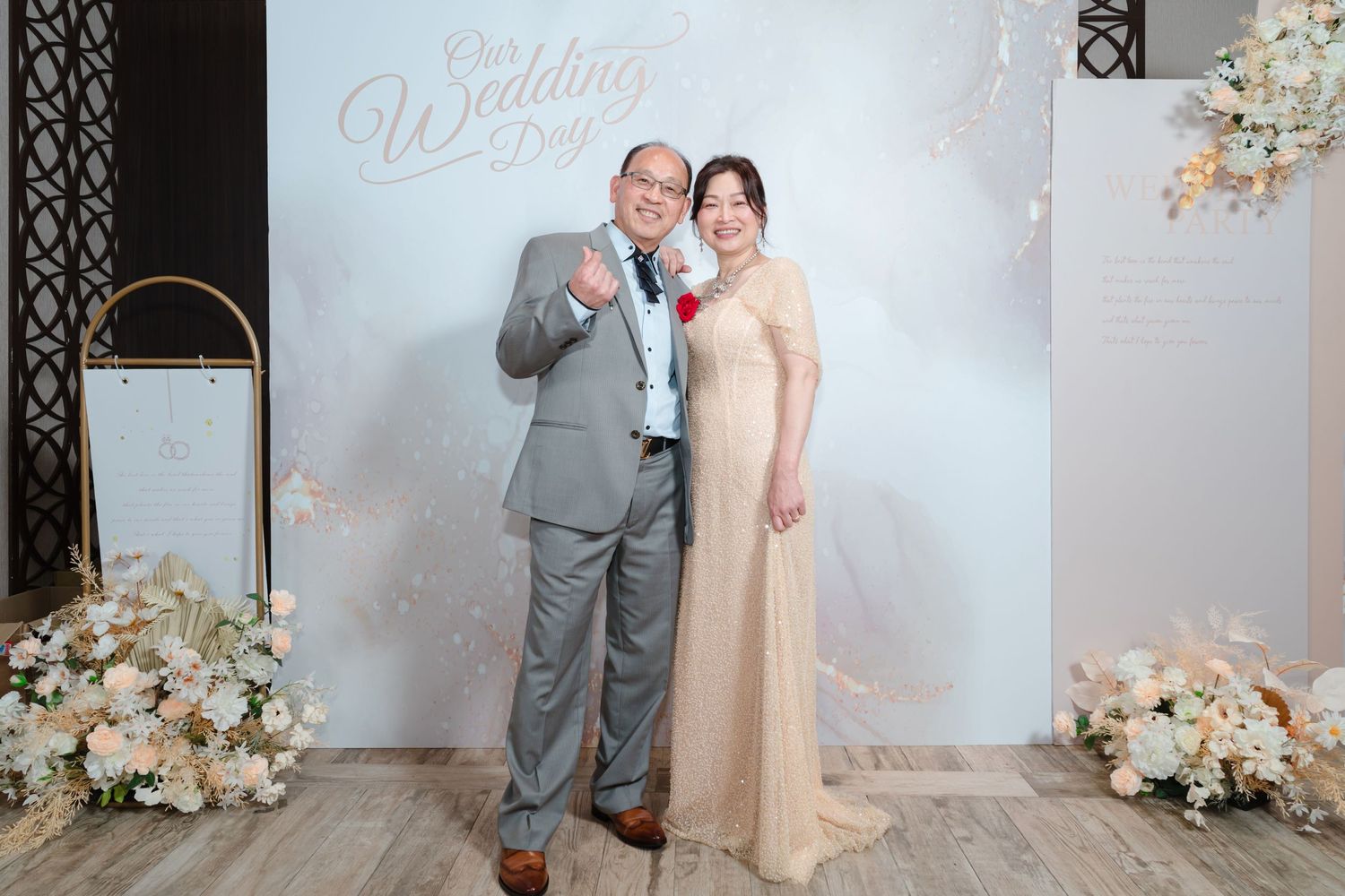 A couple poses together at an elegant wedding backdrop with floral arrangements and a white backdrop.