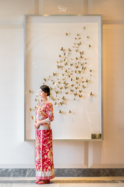 A person in a red qipao stands before a wall decorated with golden butterfly art installations.