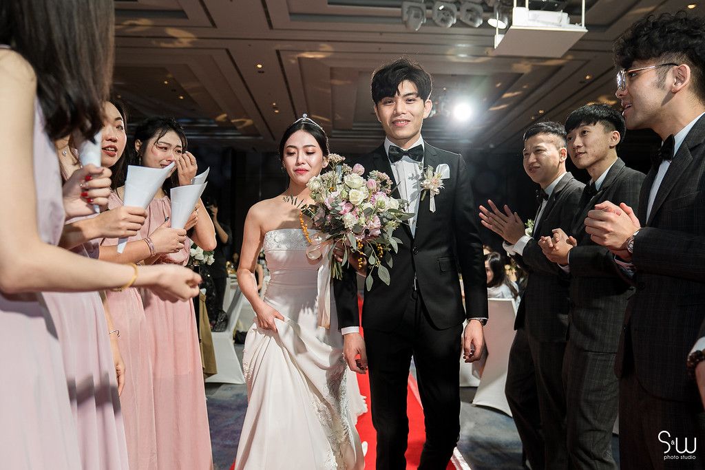 Wedding processional with couple walking through crowd of guests in formal attire.