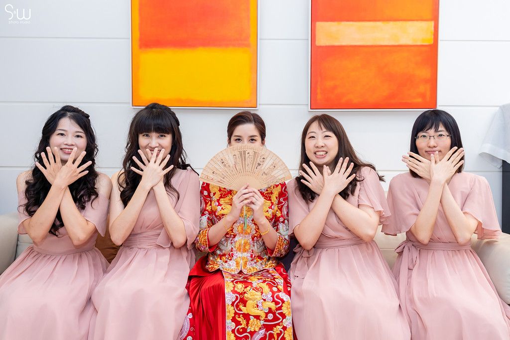Wedding party with bridesmaids in pink dresses making playful poses against orange artwork.