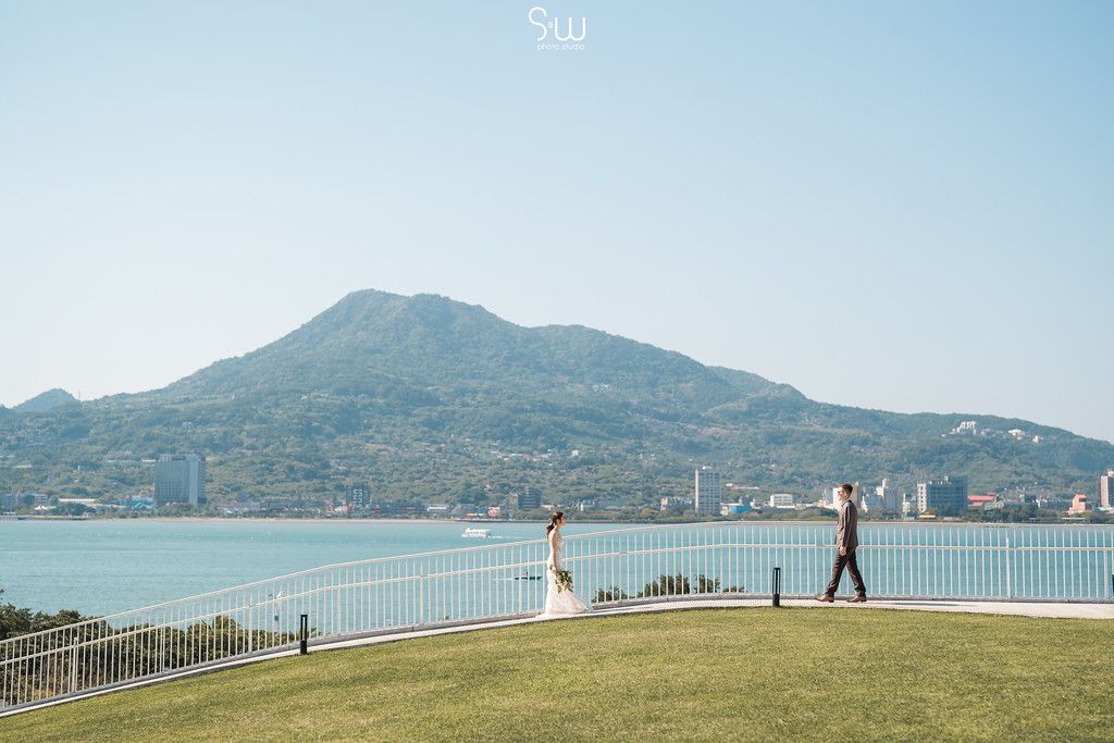 Scenic coastal wedding photo with mountain and ocean views in the background.