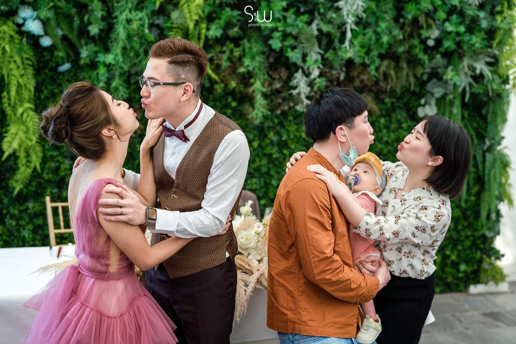 Two couples sharing intimate moments against a backdrop of lush greenery at an event.