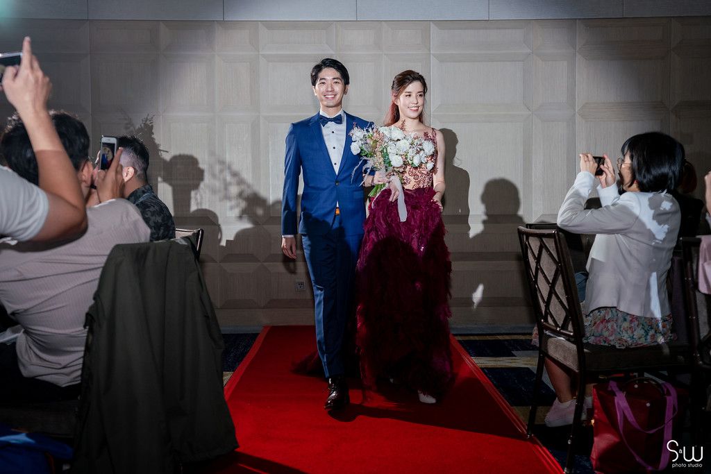 Wedding photographers capture a couple walking down a red carpet under dramatic lighting and shadows.