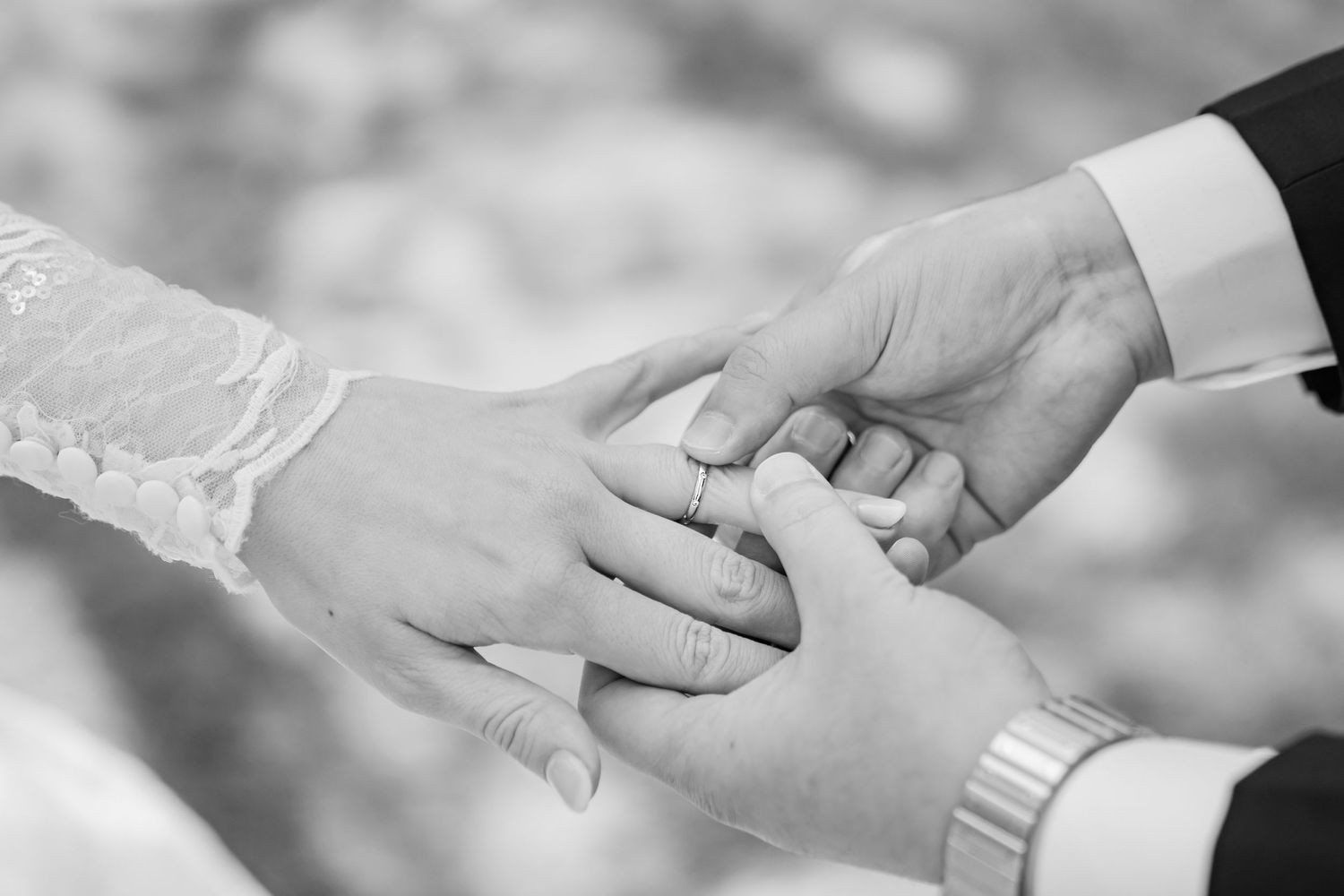 Black and white close-up of hands exchanging wedding rings during ceremony.