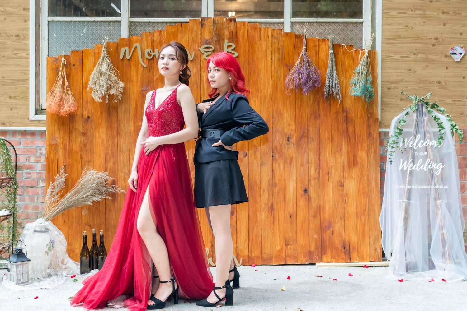 Two models pose dramatically against a wooden backdrop decorated with dried flowers and garlands.