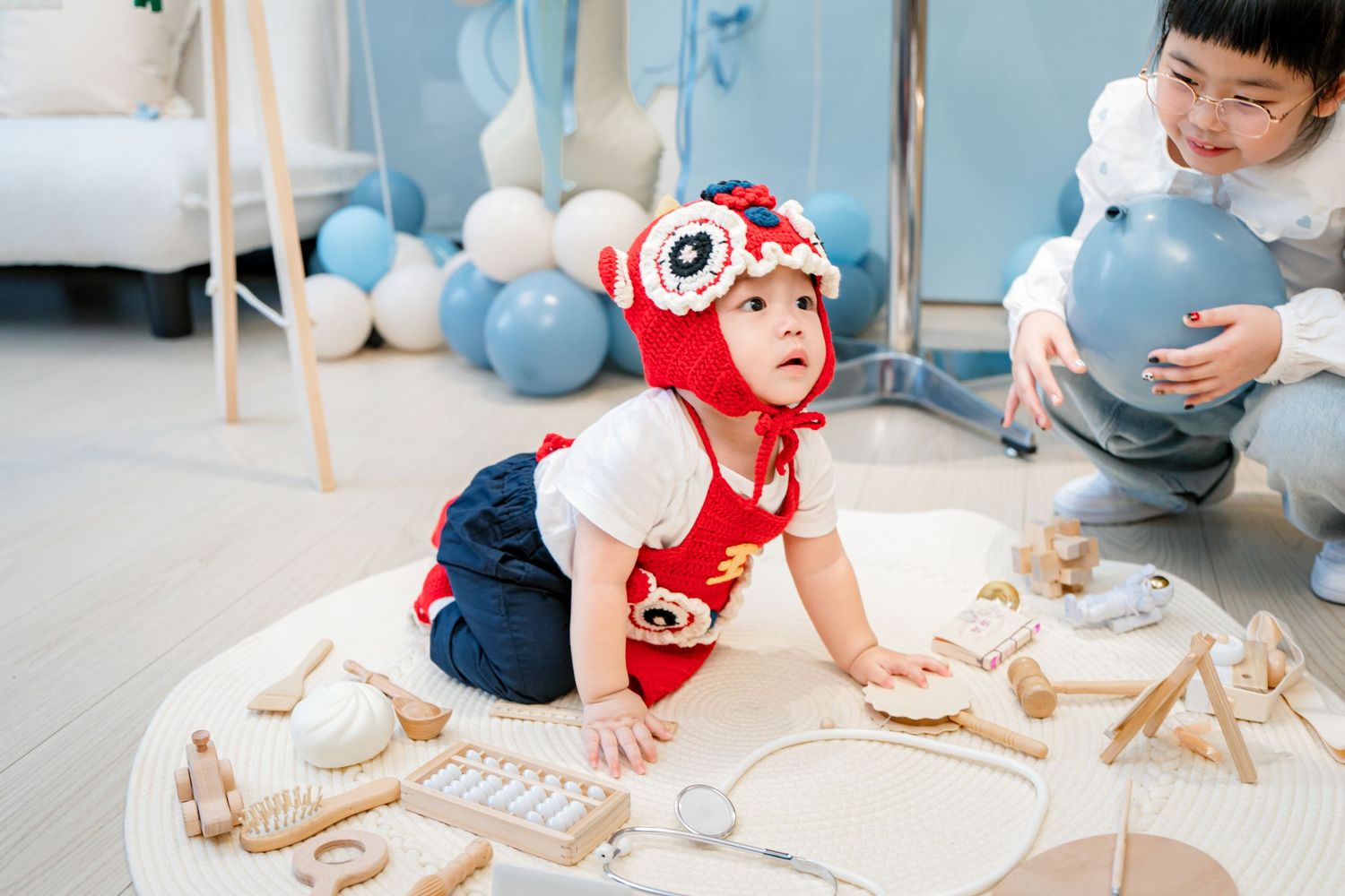 A child in a red shirt plays with wooden building blocks and toys on a light colored floor.