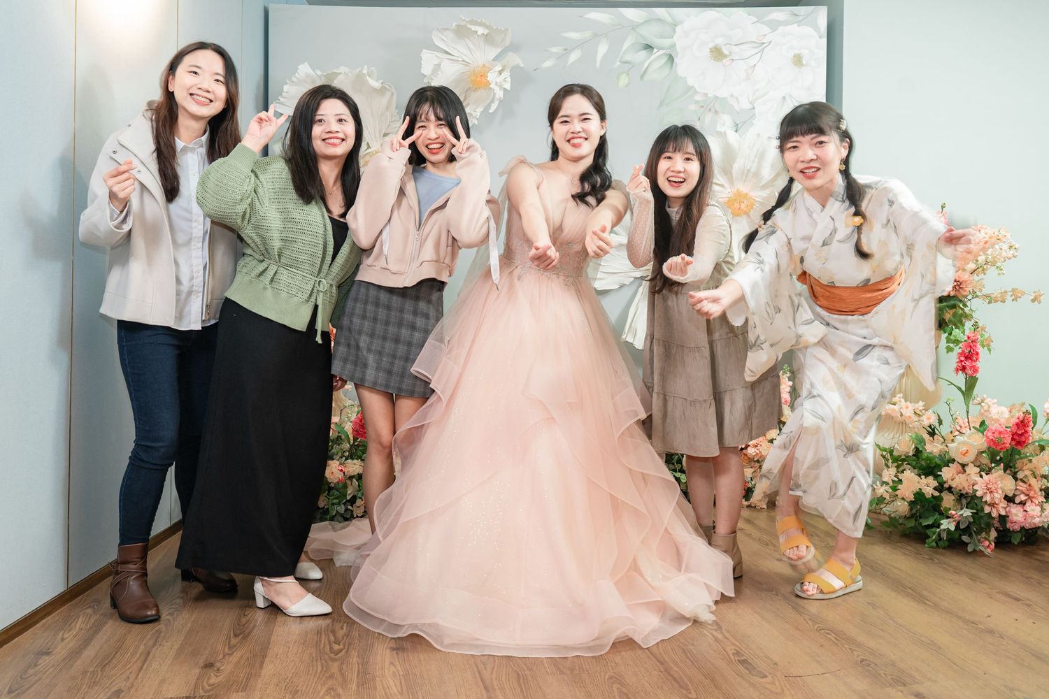 A group poses together in formal attire with pink floral decorations in the background during a special occasion.