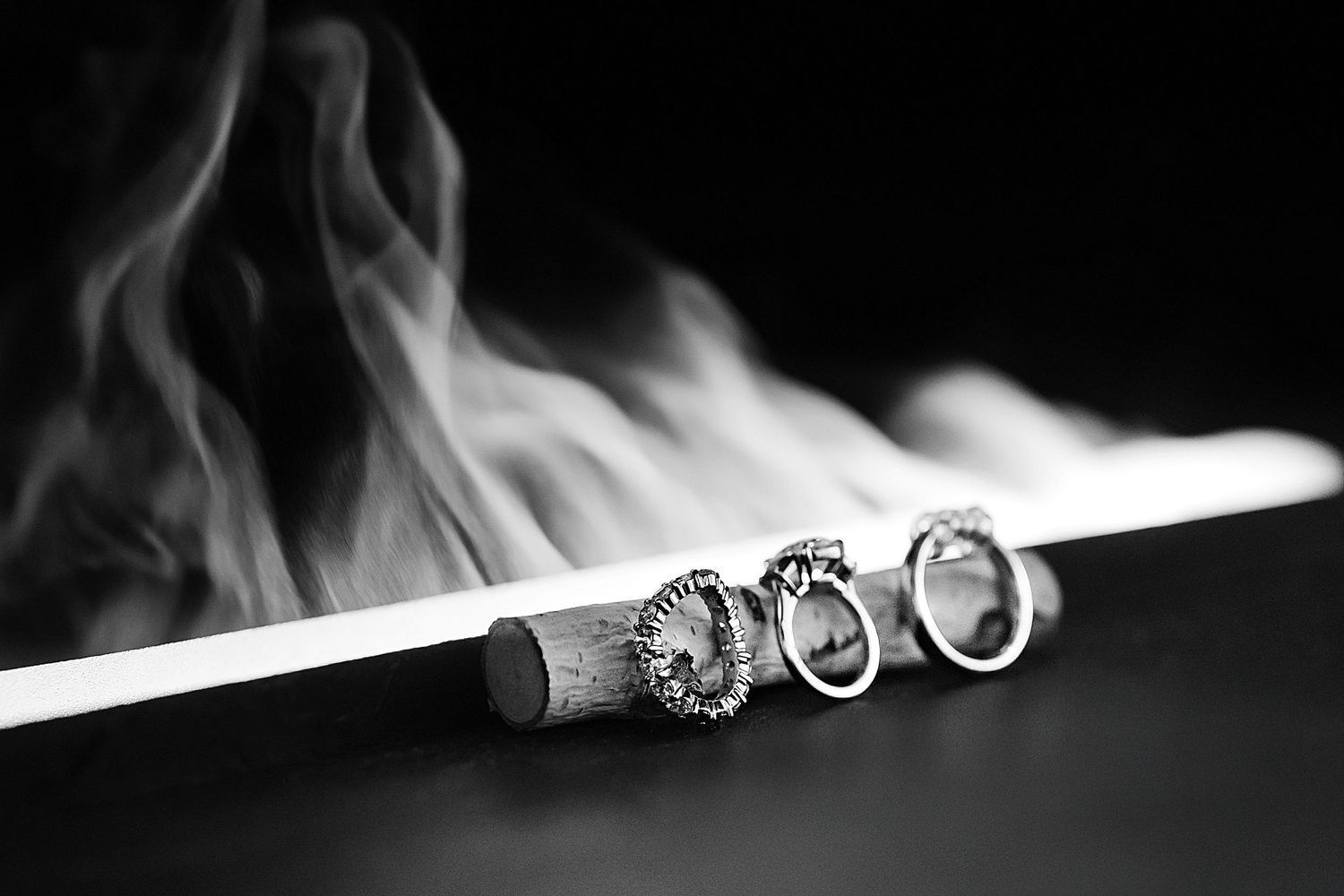 Wedding rings rest on a smoking cigarette in an artistic black and white composition.