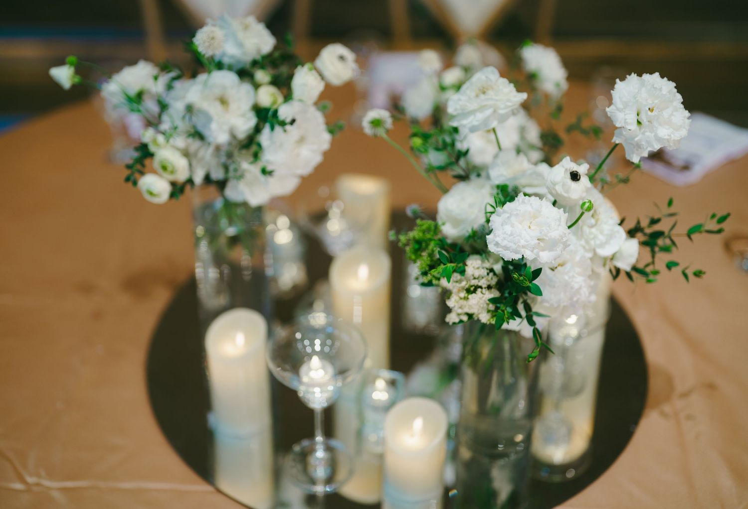 Elegant white floral wedding reception centerpieces with glowing candles in glass vases on a rustic table setting.