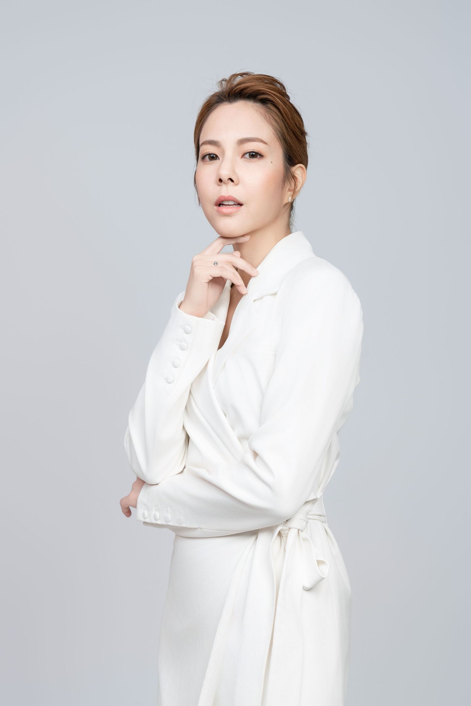 A figure in an elegant white robe poses gracefully against a light gray background in a fashion photo series.