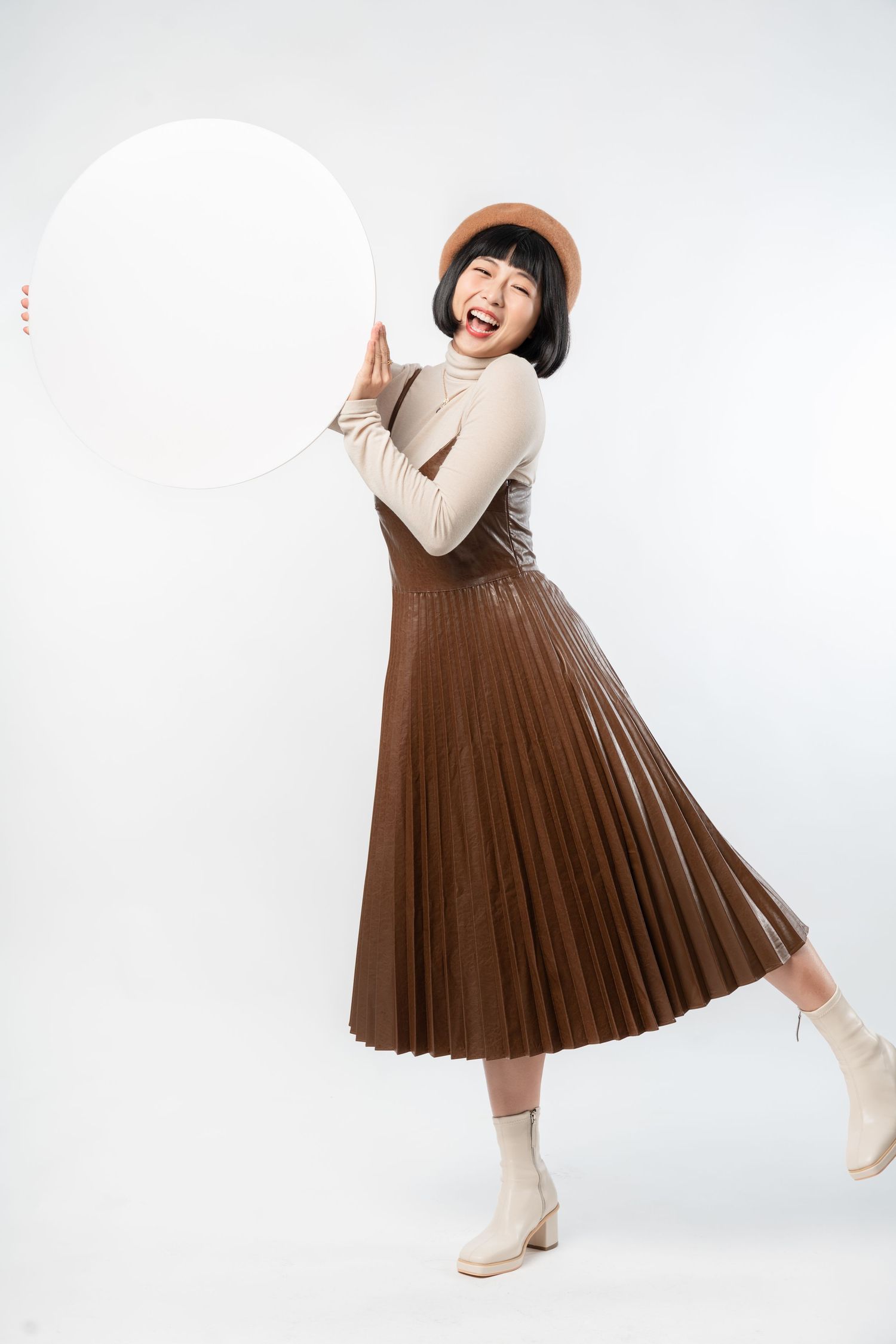 A person wearing a brown pleated midi skirt and cream sweater poses playfully in three different positions against a white backdrop.