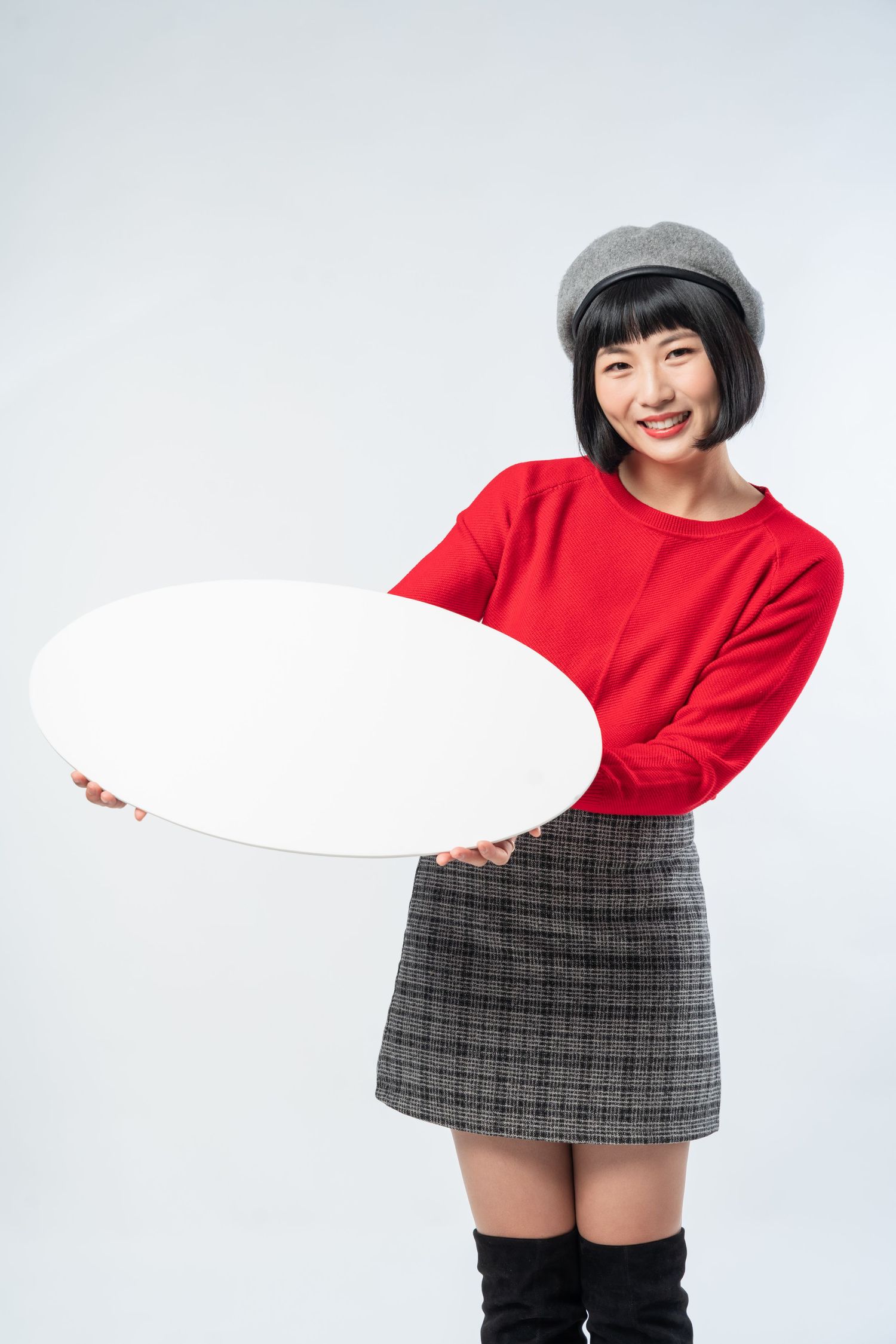 A person in a red sweater and plaid skirt holds a blank white sign while posing against a white background.