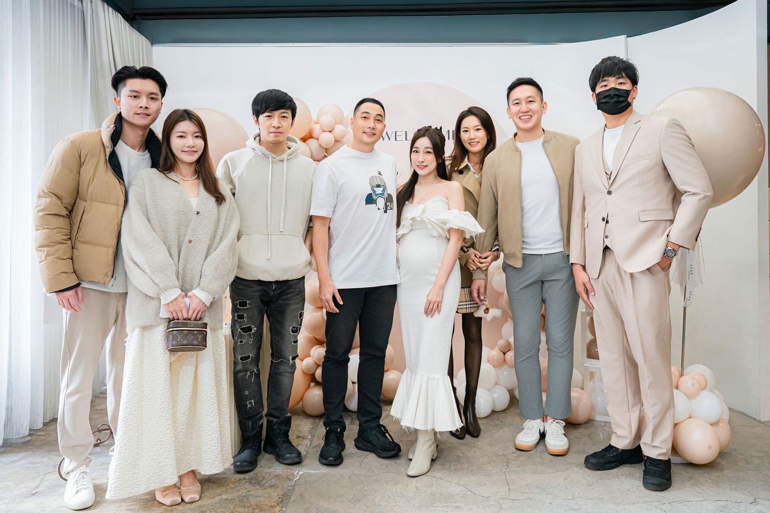 A group of people wearing coordinated beige and cream colored outfits pose together in a bright indoor setting.