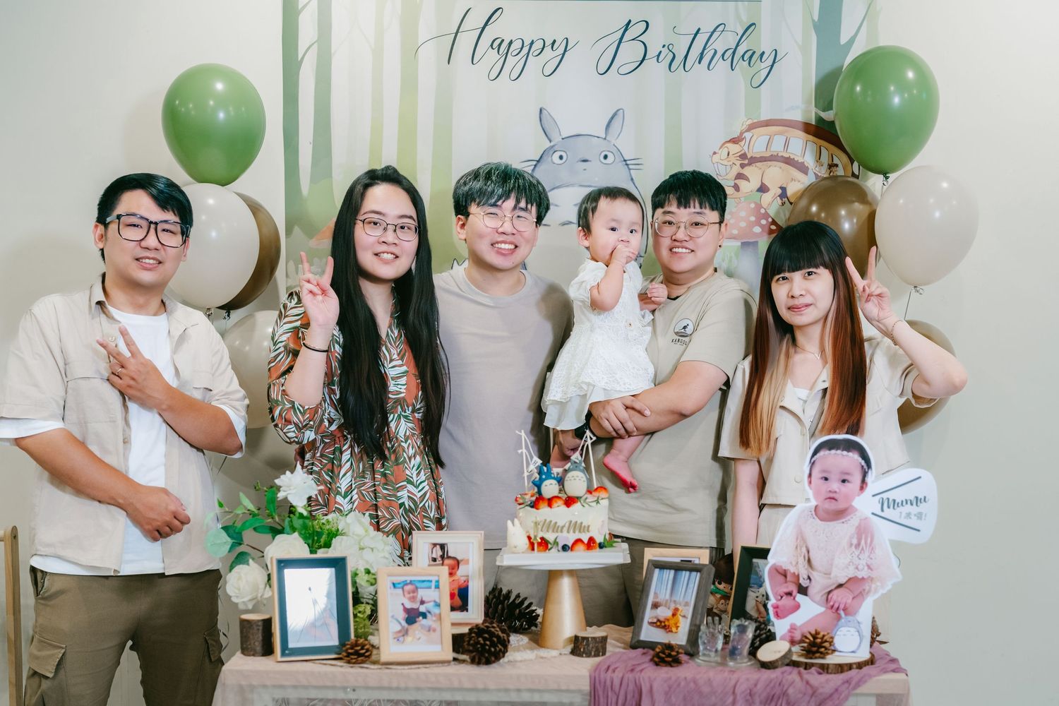 A birthday party setup with green balloons, cake, decorations and a group gathering to celebrate the occasion.