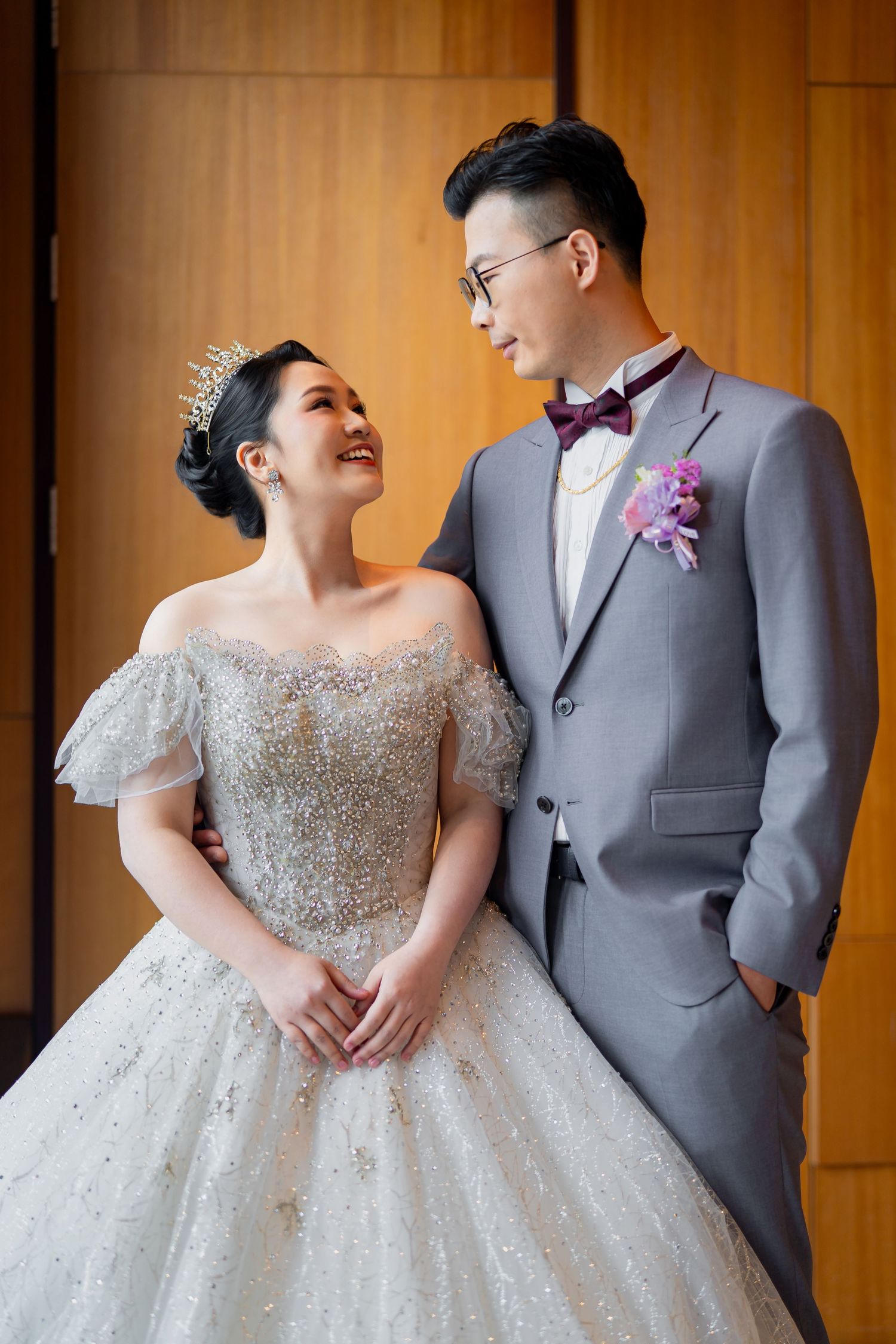 A romantic wedding moment between a couple in grey tuxedo and sparkly white ballgown captured in warm lighting.